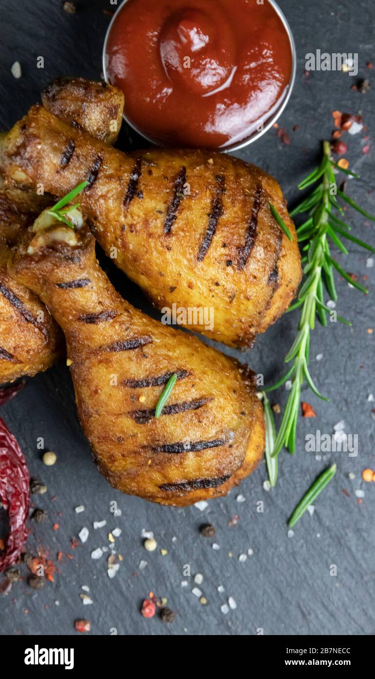 gambe di pollo alla griglia con salsa rossa su una superficie di pietra nera Foto Stock