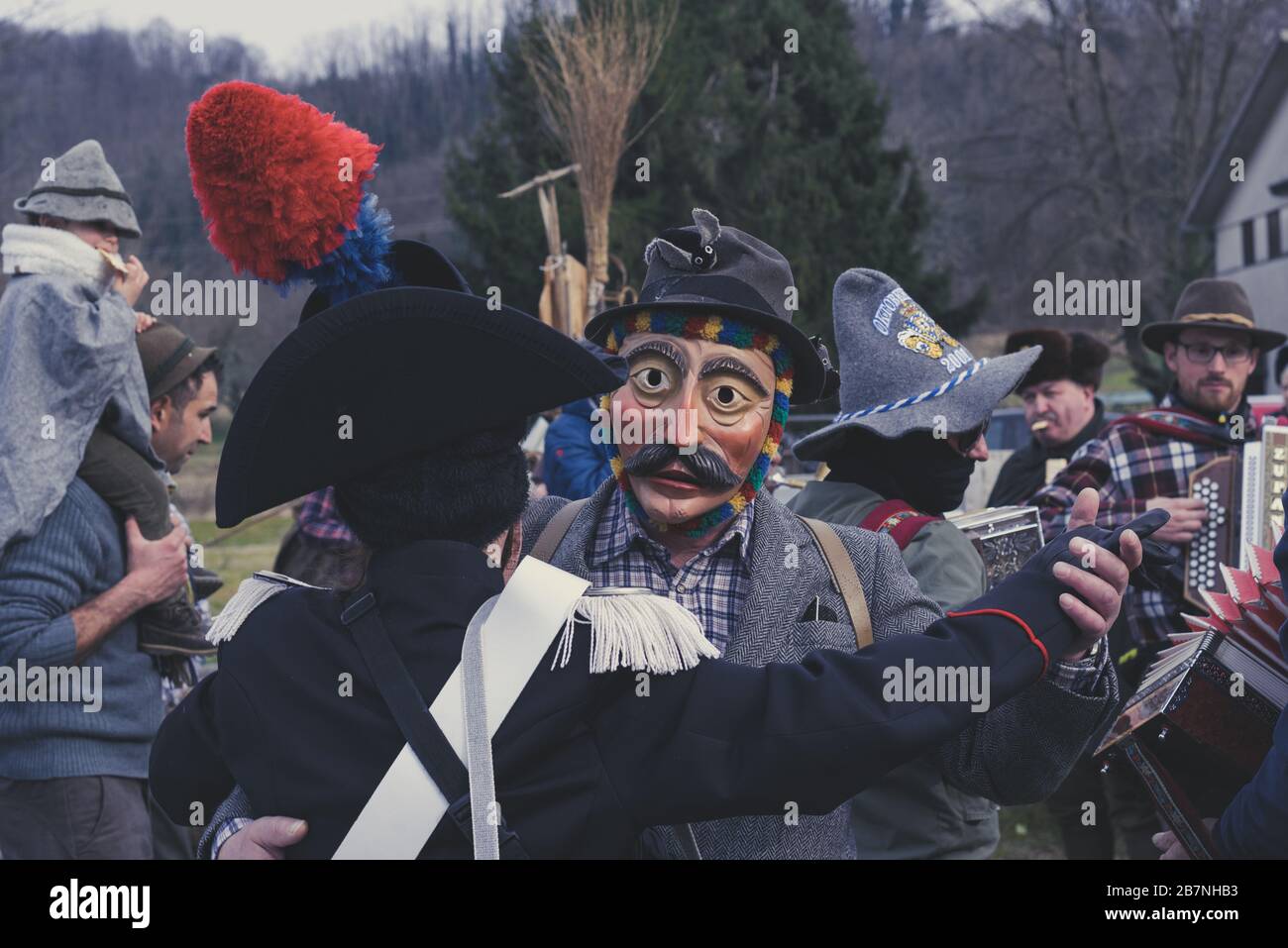 Due uomini mascherati che ballano con un gruppo tradizionale sullo sfondo. Concetto di musica folk. Sfilata di carnevale di Pust. Foto Stock