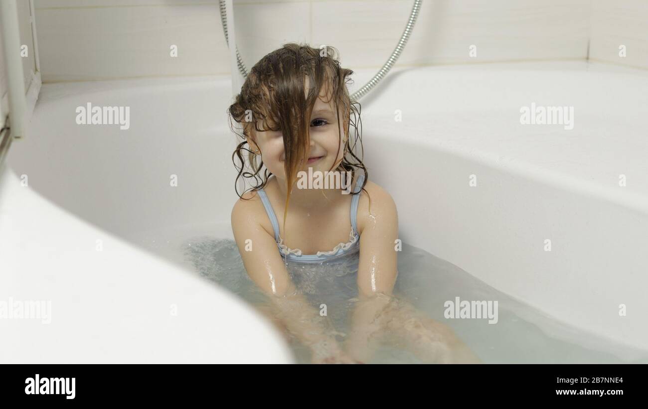 Attraente ragazza di quattro anni prende un bagno con schiuma bagno in costume da bagno. Lava la testa. Capelli bagnati. Igiene per il bambino biondo carino. Ragazza carina sorridente. Bambino piccolo, 4-5 anni bionda ragazza in bagno Foto Stock