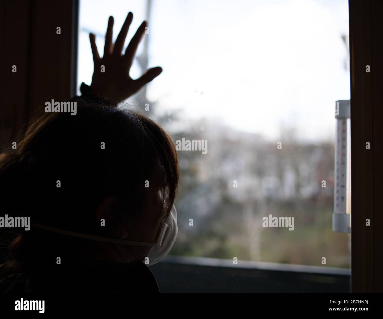 donna in una maschera protettiva guarda fuori la finestra a casa, tempo di quarantena Foto Stock