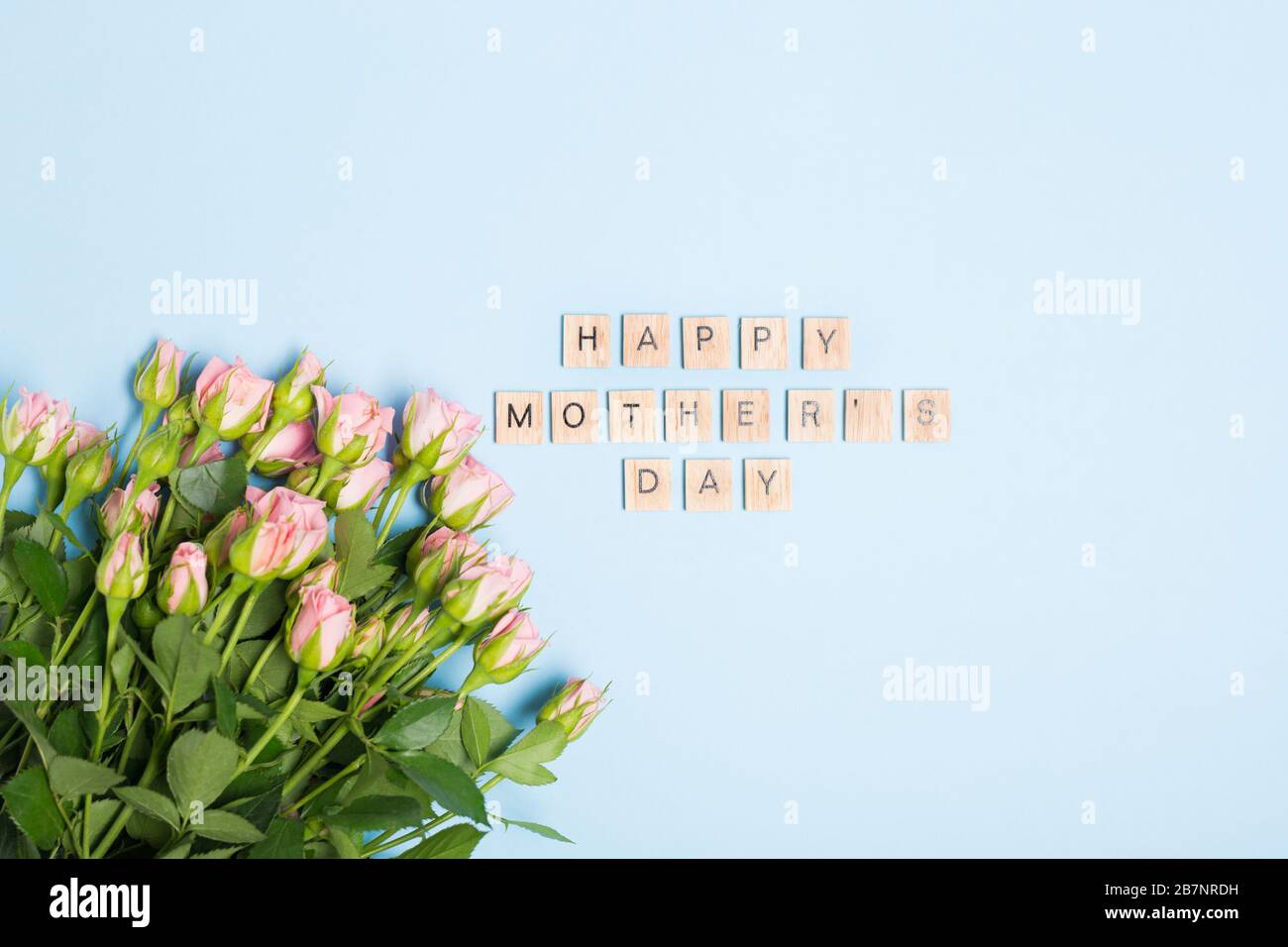 Testo del giorno della madre felice e rose rosa su sfondo blu. Spazio libero. Disposizione piatta. Vista dall'alto. Foto Stock