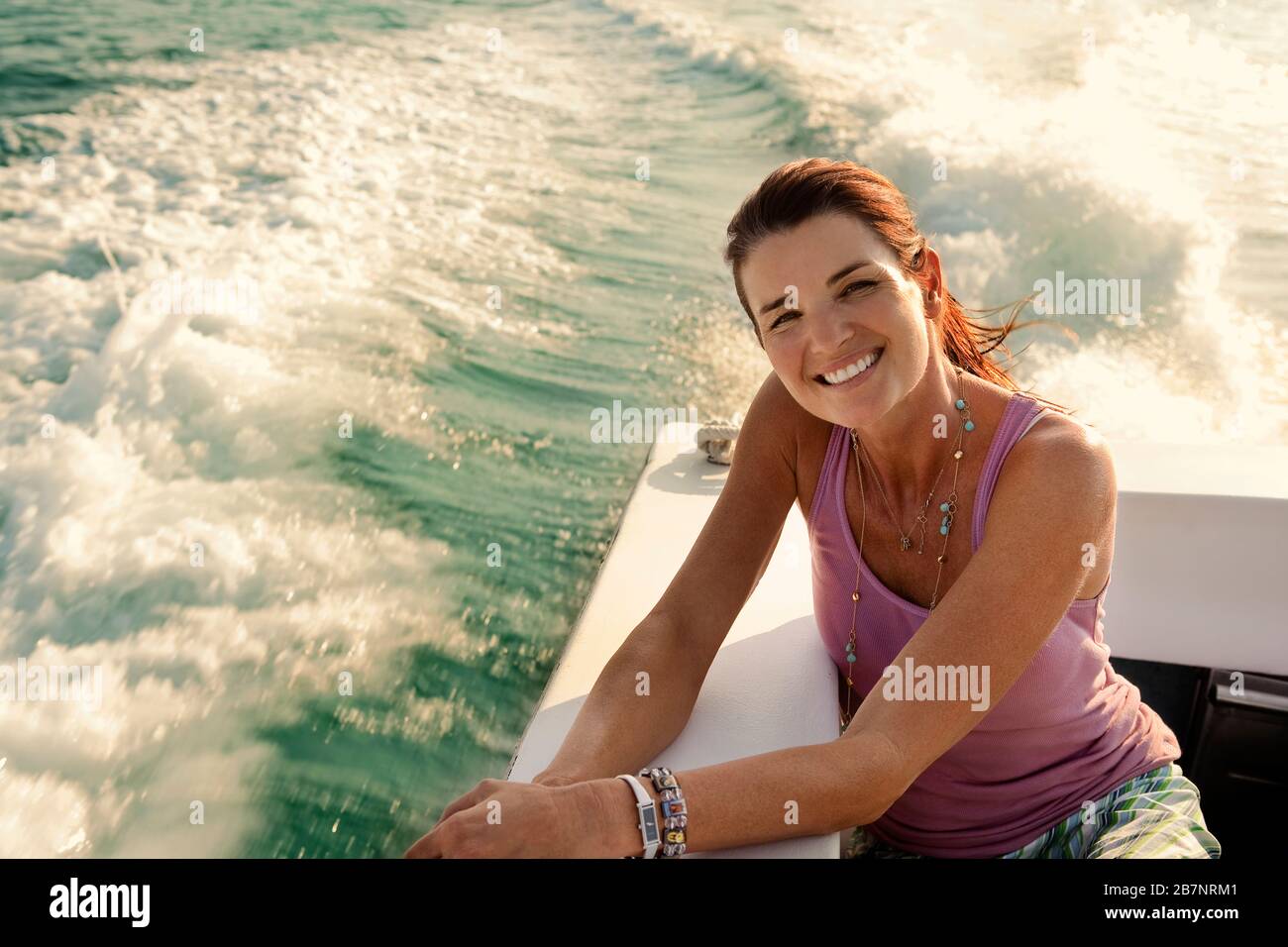 Ritratto di donna sorridente di mezza età che corre sul retro di una barca al sole. Foto Stock