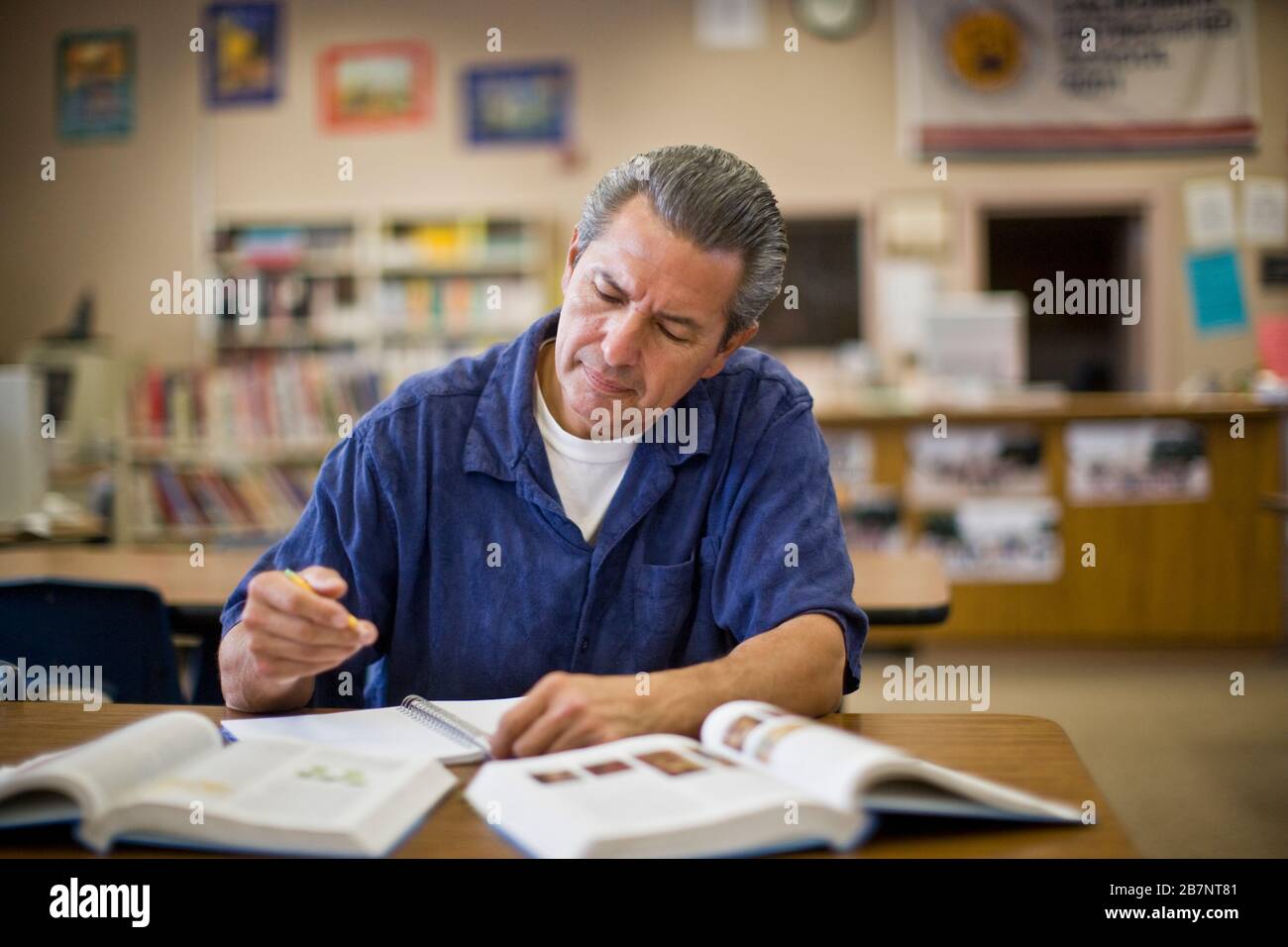 Uomo maturo che lavora a scuola a una scrivania all'interno di un'aula. Foto Stock