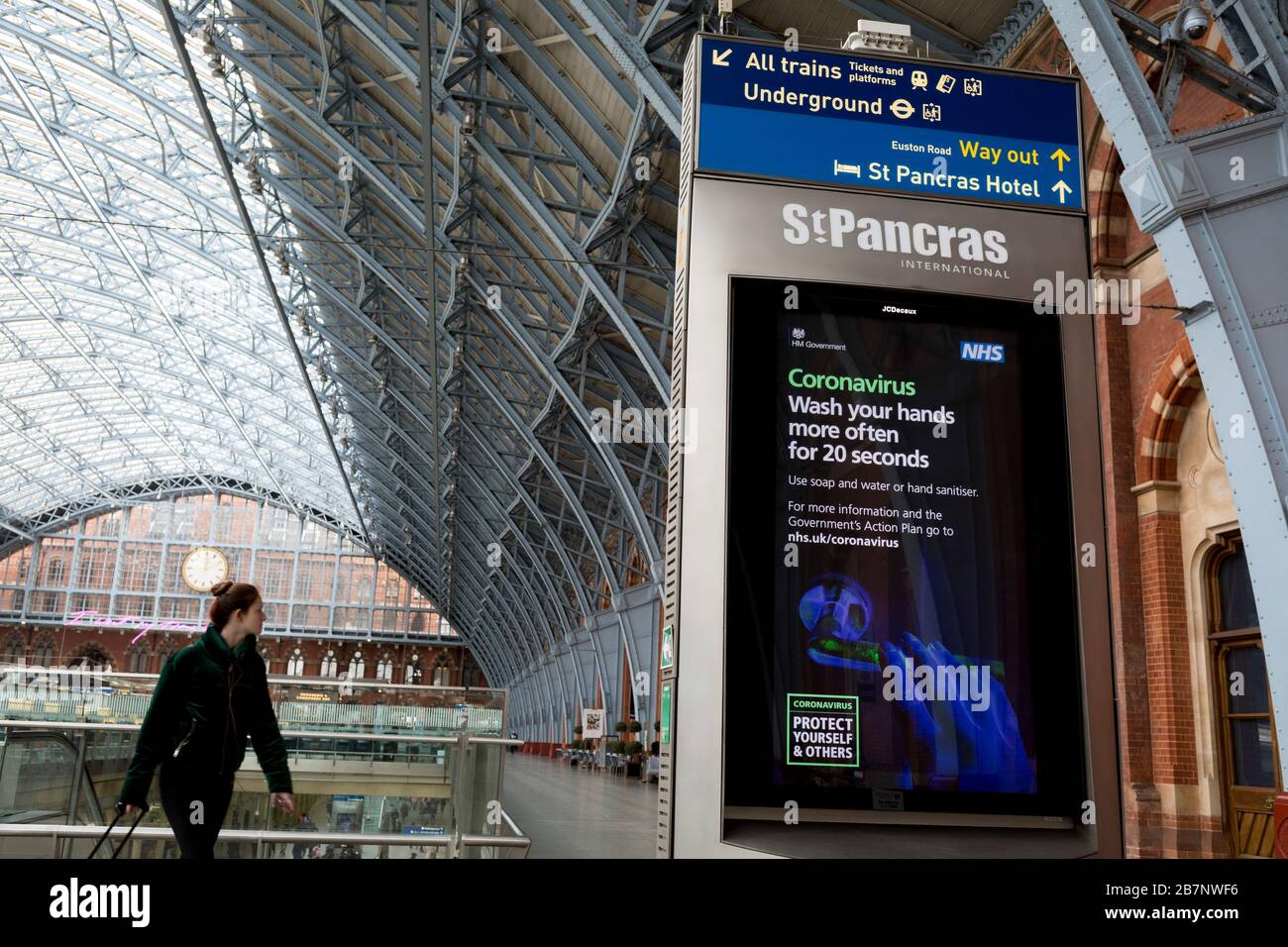 Come il governo britannico ha esortato tutti i britannici a evitare viaggi non essenziali all'estero per combattere la pandemia di Coronavirus in Gran Bretagna, i passeggeri delle ferrovie passano attraverso un annuncio digitale di informazione pubblica da parte del governo e il NHS (National Health Service) dice al pubblico di lavarsi le mani in modo approfondito, In un atrio insolitamente tranquillo nella stazione ferroviaria di St. Pancras, il 17 marzo 2020, a Londra, Inghilterra, il capolinea londinese dei servizi Eurostar per l'Europa continentale. Foto Stock
