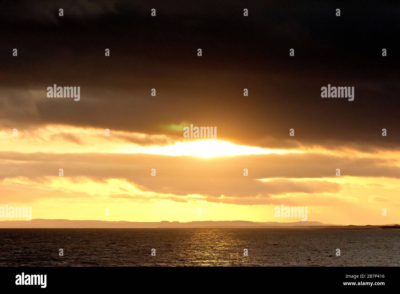 Verso la fine della giornata, il sole si rompe finalmente attraverso i cieli grigi di piombo per offrire un tramonto spettacolare. Foto Stock