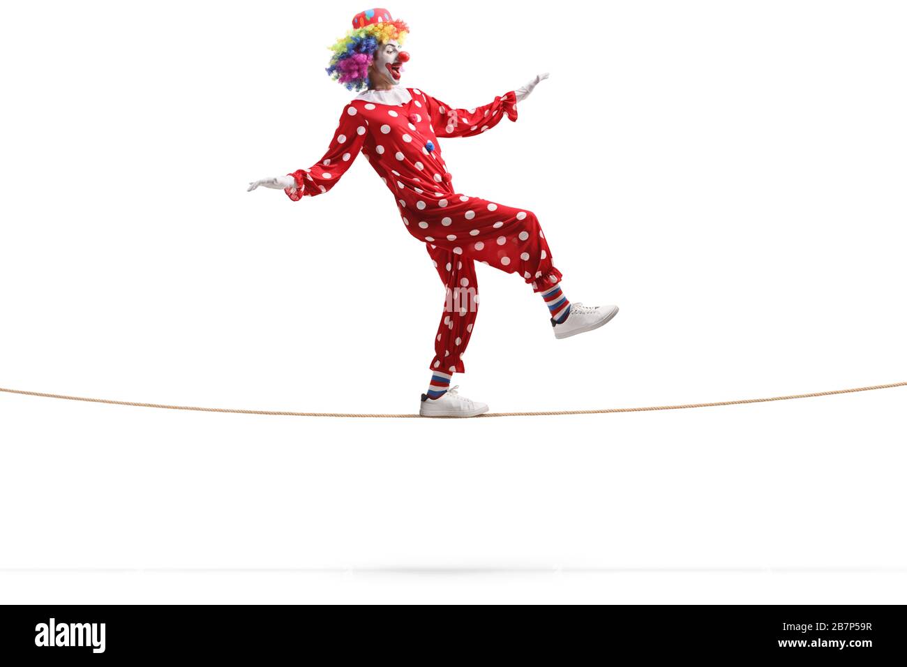 Scatto di profilo a tutta lunghezza di un clown che cammina su una corda isolata su sfondo bianco Foto Stock