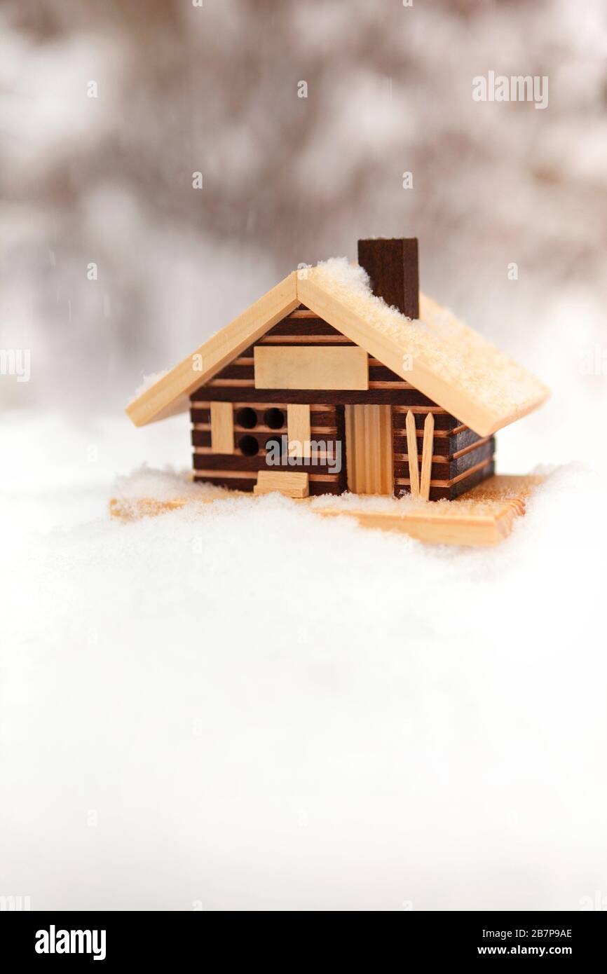 Piccolo modello di casa in legno tra neve con nevicata e sfondo offuscato foresta invernale Foto Stock