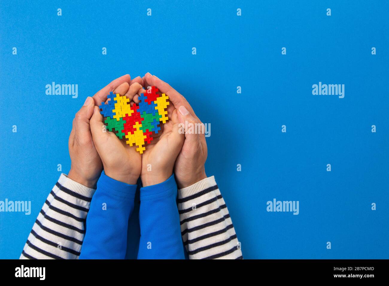 Concetto del giorno di consapevolezza di autismo del mondo. Mani per adulti e bambini che tengono il cuore del puzzle su sfondo blu chiaro Foto Stock