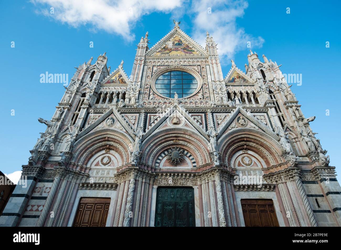 Si affaccia sull'esterno frontale decorato della Cattedrale di Siena. Intricate pietre, colorate immagini religiose e cielo blu riflesso nella rosetta Foto Stock