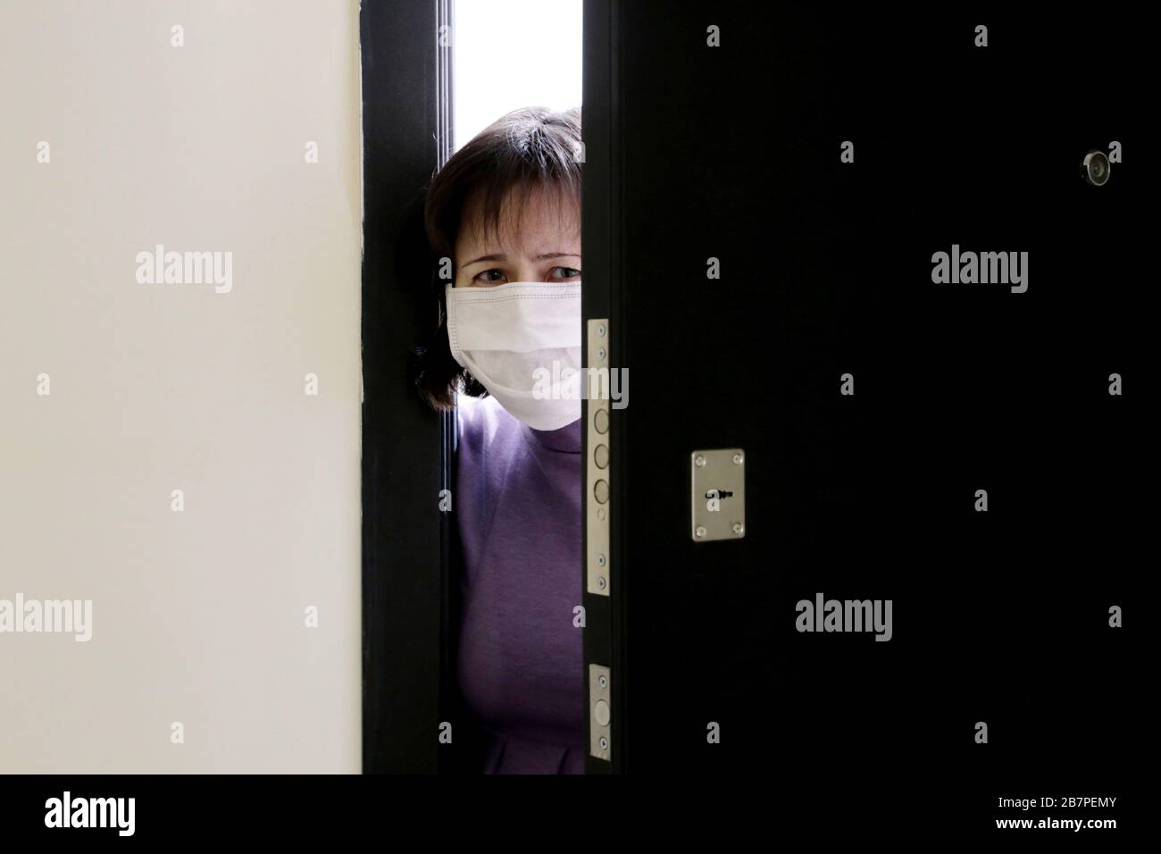 Quarantena domestica durante l'epidemia di coronavirus COVID-19. Donna preoccupata in una maschera medica in piedi nella porta aperta Foto Stock