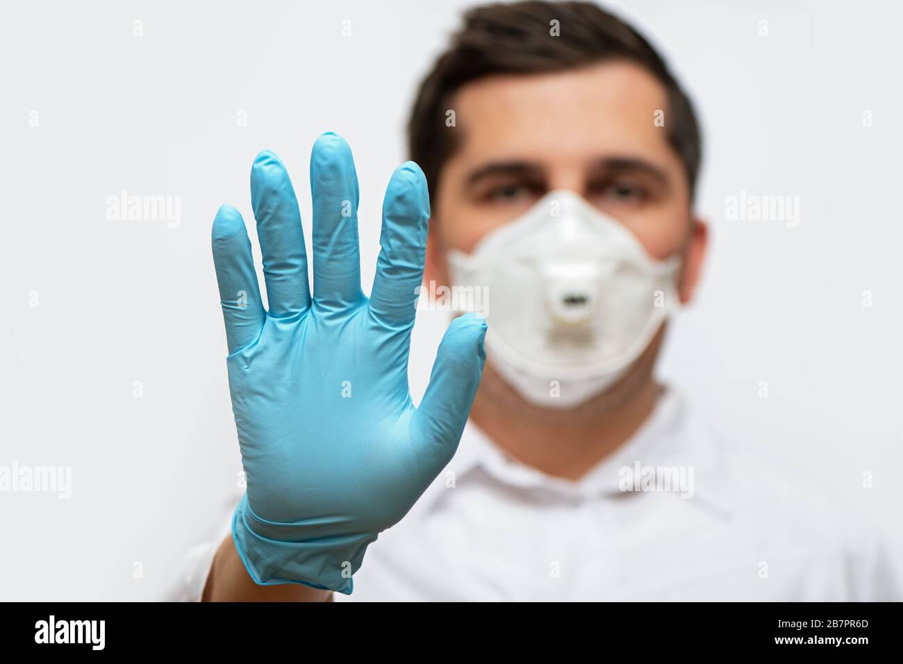 Ritratto del medico in uniforme medica con maschera facciale protettiva e una mano con guanti che mostra un segnale di stop. Interrompere il concetto COVID-19. Foto Stock