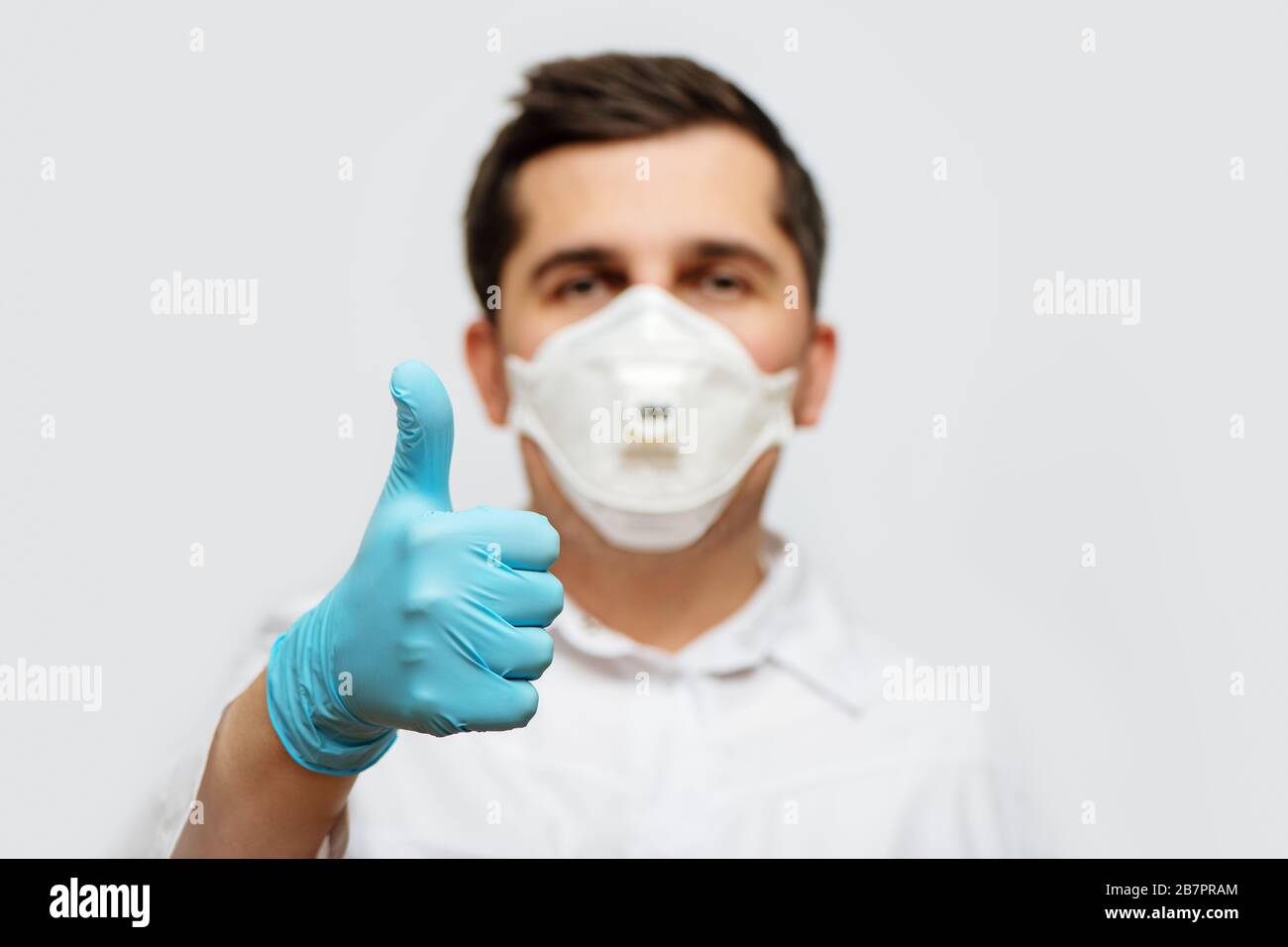 Ritratto del medico in uniforme medica con maschera facciale protettiva e una mano con i guanti che danno i pollici in su. Interrompere il concetto COVID-19. Foto Stock
