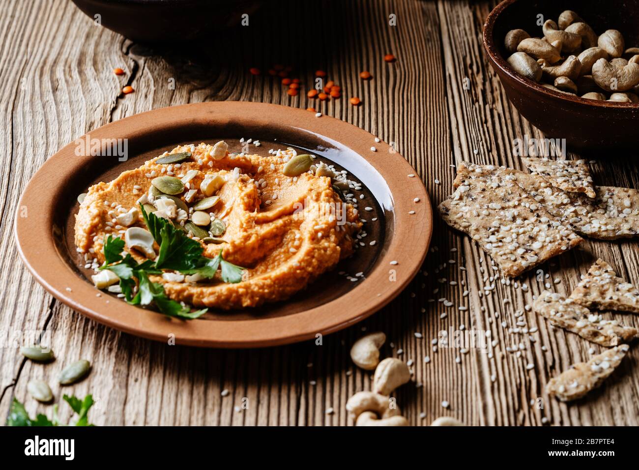 Snack salutari, tuffo gourmet. Hummus di lenticchie, semi di sesamo e semi di girasole su un tavolo di legno rustico Foto Stock