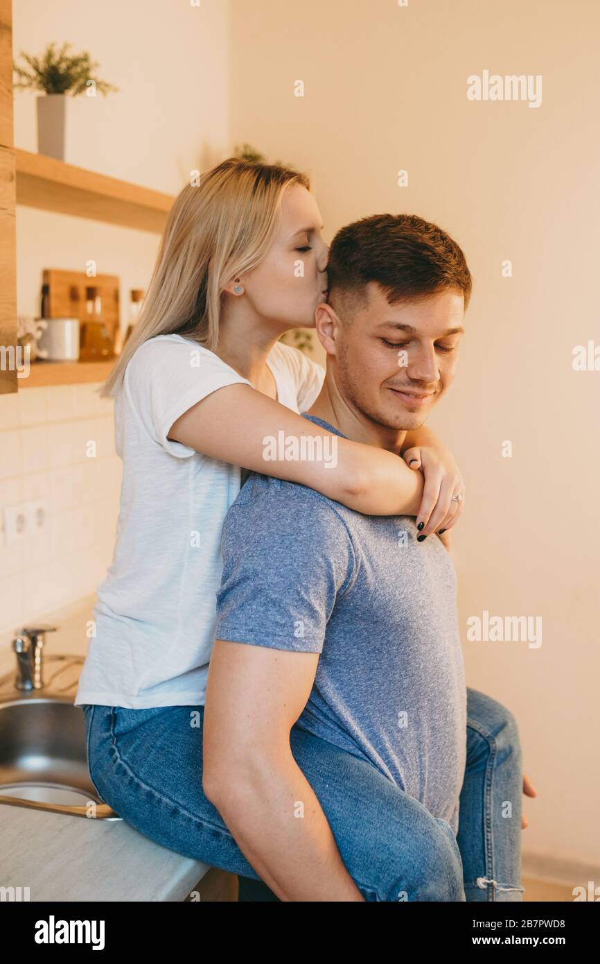 Affascinante signora bionda caucasica abbracciando il suo amante e baciandolo in cucina Foto Stock