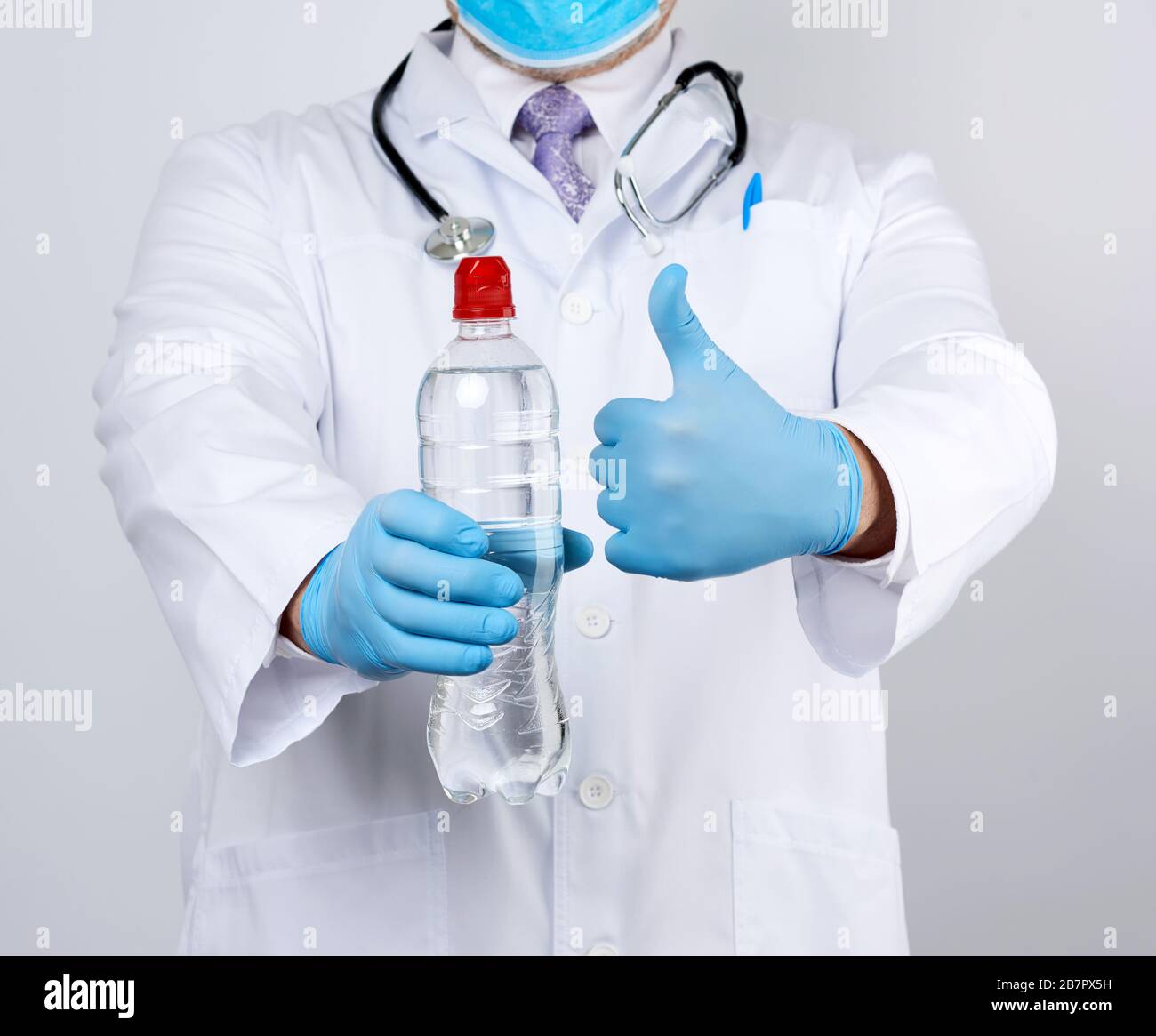 medico in un cappotto bianco e guanti in lattice blu contiene una bottiglia trasparente di acqua, è necessario consumare più acqua per sentirsi meglio Foto Stock