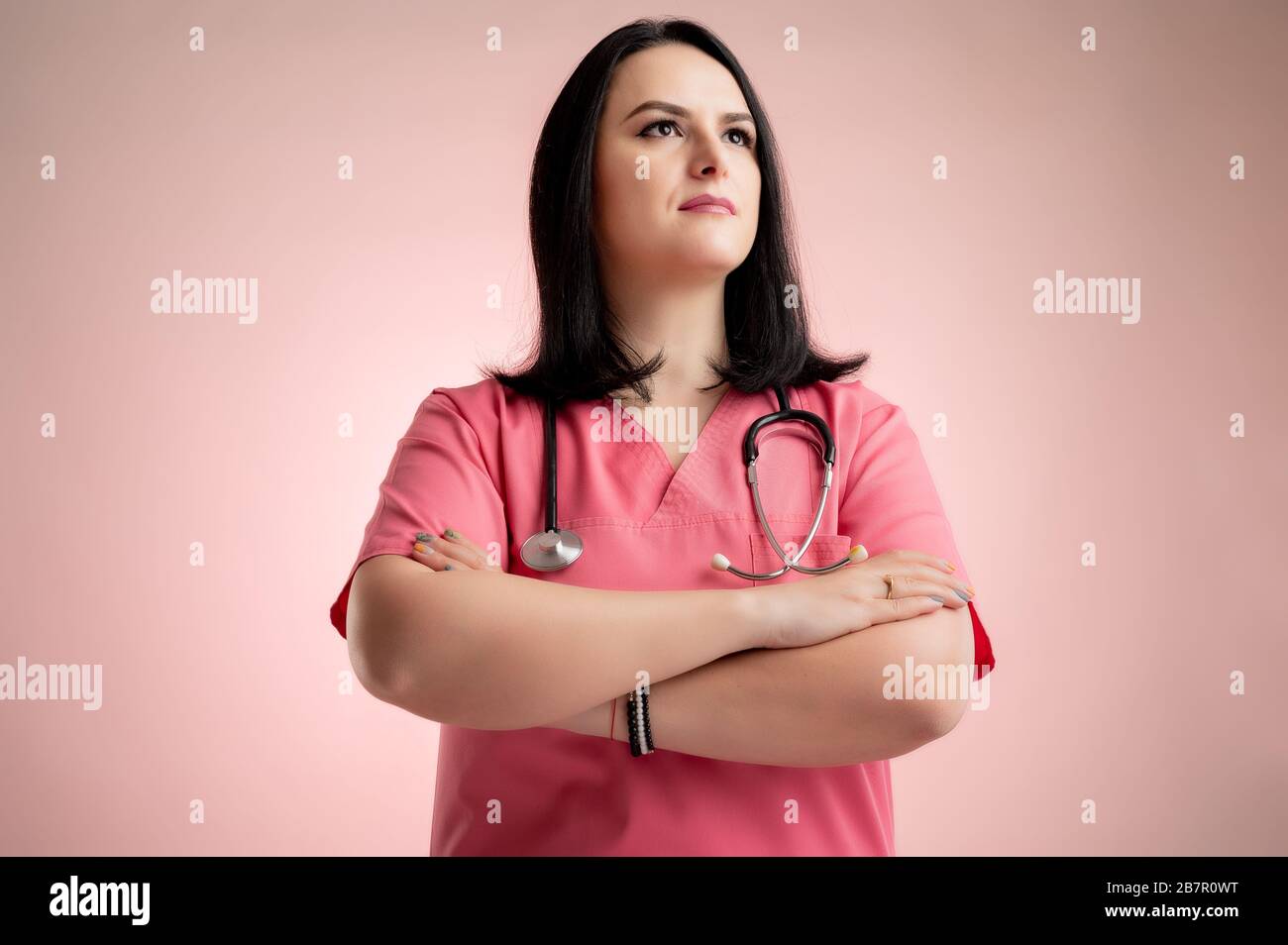 Ritratto di una bella donna medico con stetoscopio che indossa scrub rosa, cercando fiducioso eroe-shot in posa su un rosa isolato backround. Foto Stock