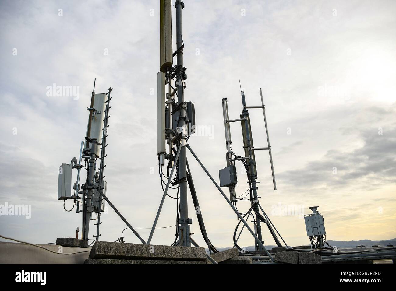 Antenna di rete per telecomunicazioni cellulari montata su un palo metallico che fornisce forti onde di segnale dalla parte superiore del tetto attraverso la grande città Foto Stock