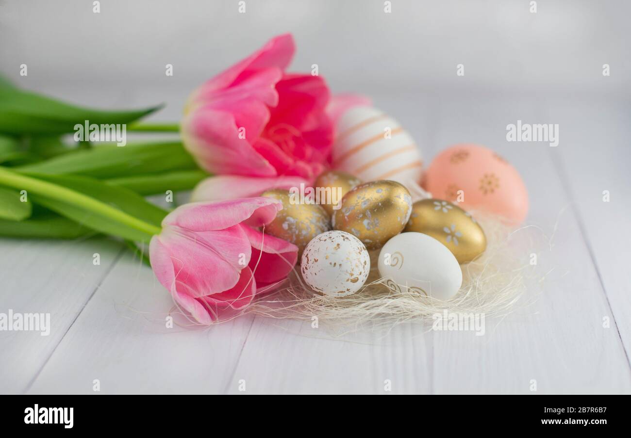 Uova dorate per le vacanze di Pasqua in aprile con fiori di tulipani Foto Stock