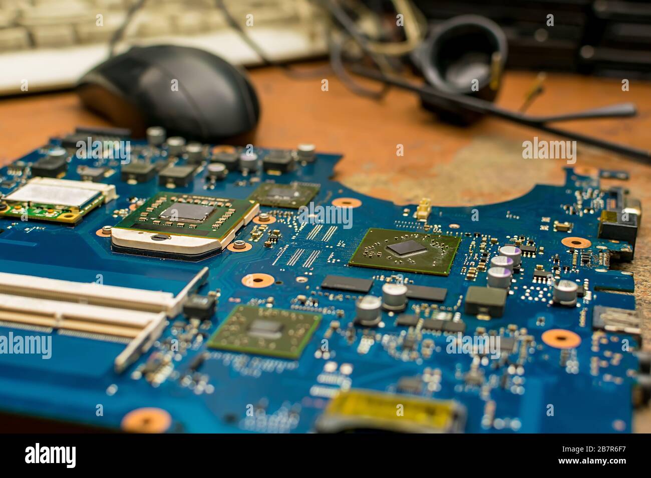 la scheda madre del computer si trova su un vecchio tavolo di riparazione in legno usurato del centro di assistenza sullo sfondo di strumenti, un mouse per computer Foto Stock