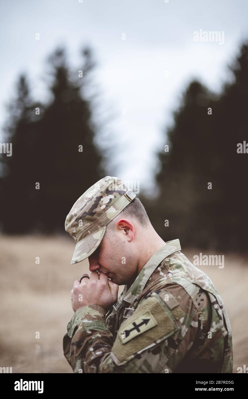 Messa a fuoco superficiale ripresa verticale di un giovane soldato che prega un campo Foto Stock