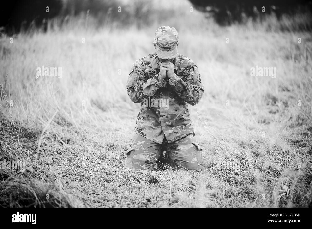 Colpo in scala di grigi di un soldato americano che prega in un campo mentre si inginocchiano su un'erba asciutta Foto Stock
