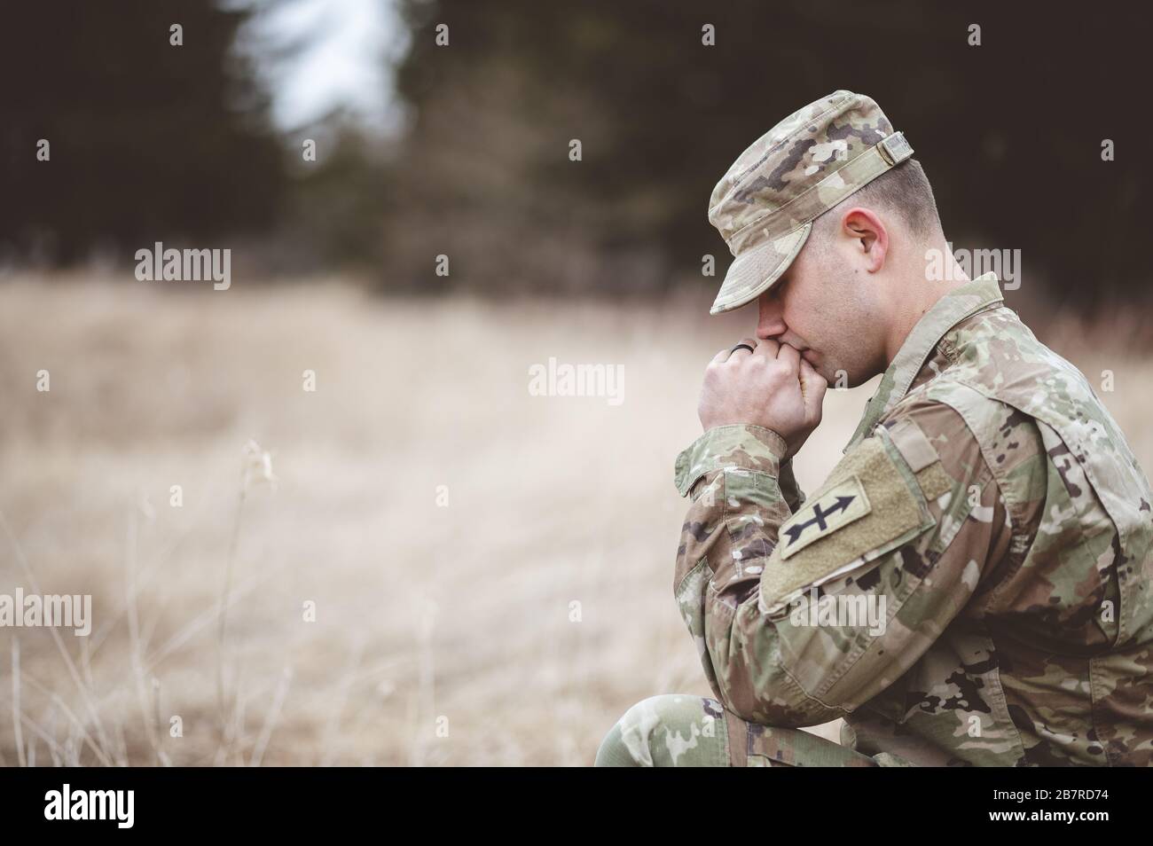 Messa a fuoco poco profonda di un giovane soldato che prega in un campo Foto Stock