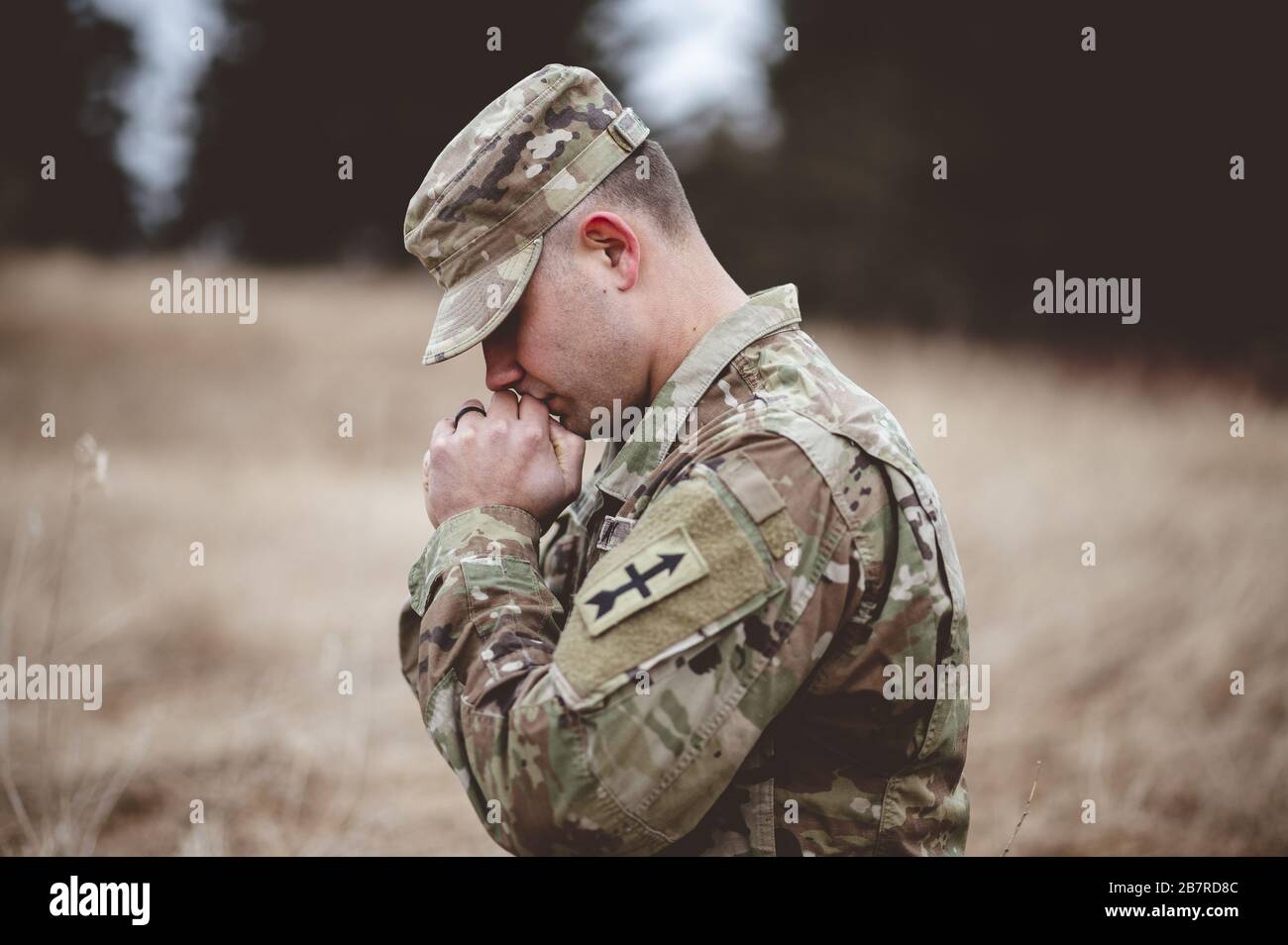 Messa a fuoco poco profonda di un giovane soldato che prega in un campo Foto Stock