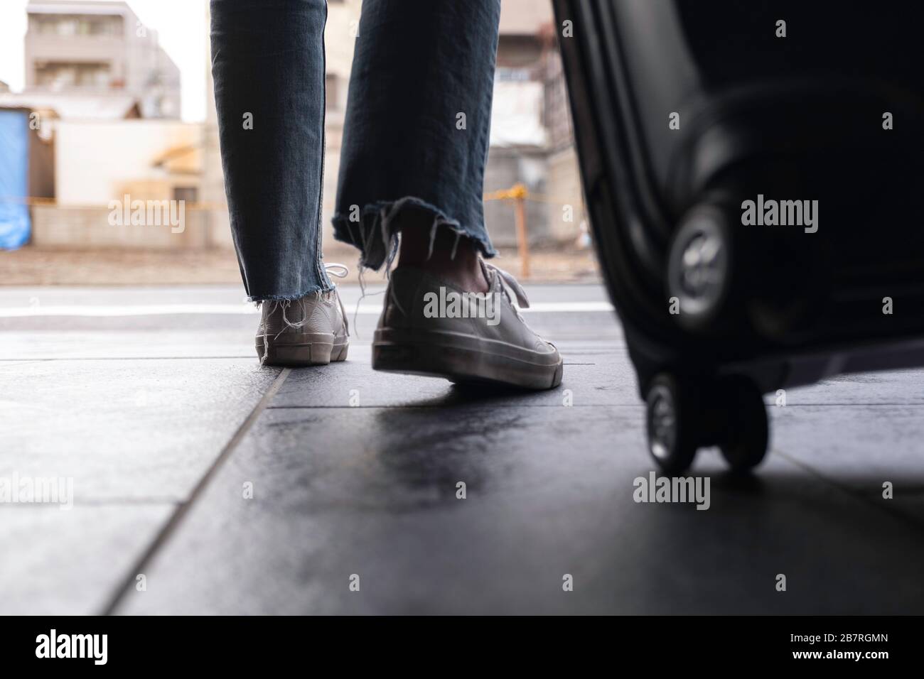 Immagine di primo piano dei piedi di una donna mentre si viaggia e trascinando un bagaglio nero all'aperto Foto Stock