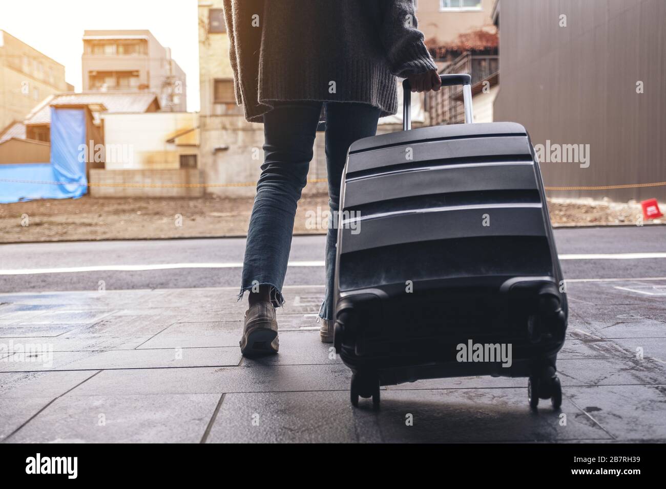 Immagine di primo piano di una donna che cammina mentre viaggia e trascina un bagaglio nero all'aperto Foto Stock