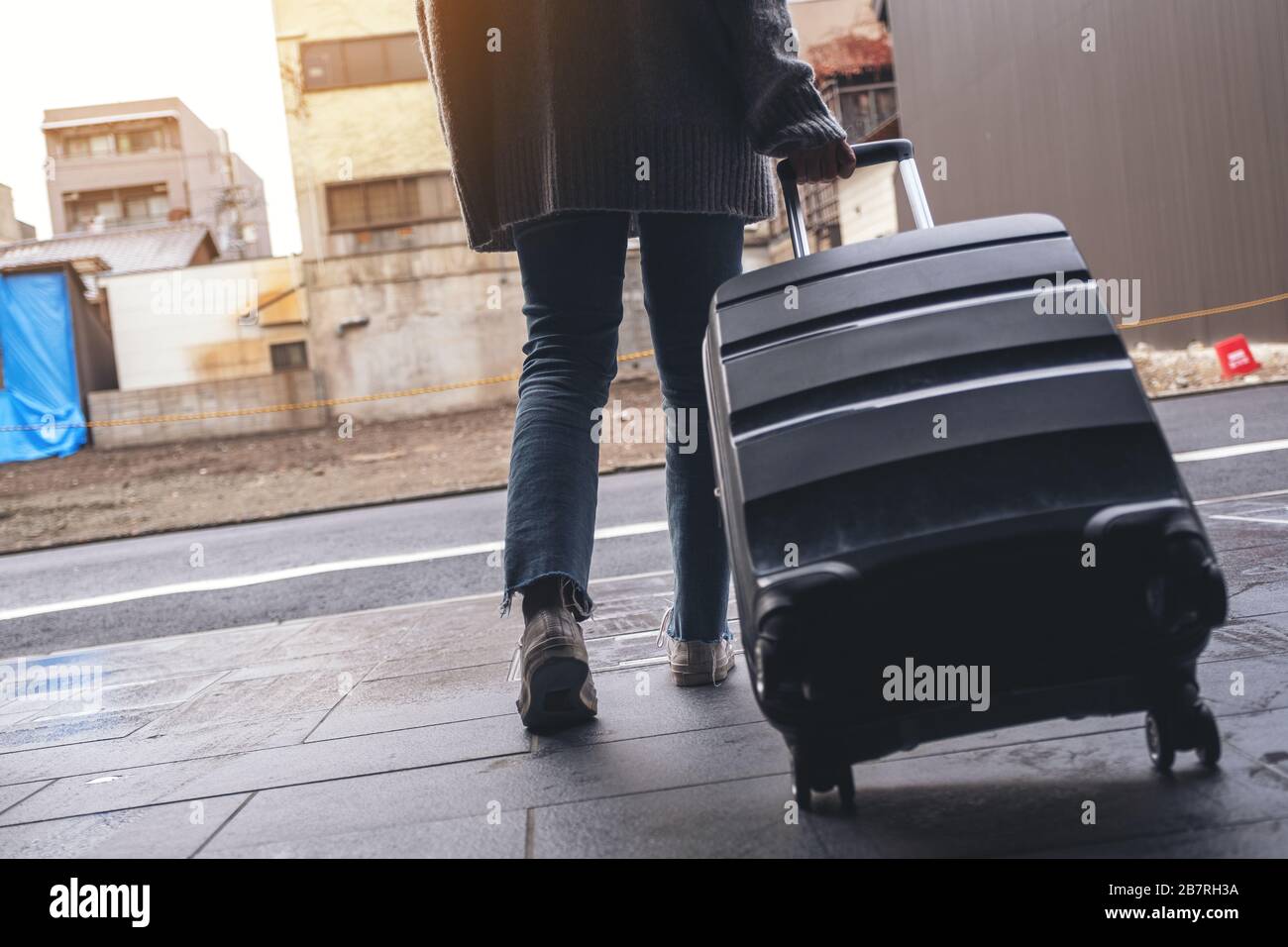 Immagine di primo piano di una donna che cammina mentre viaggia e trascina un bagaglio nero all'aperto Foto Stock