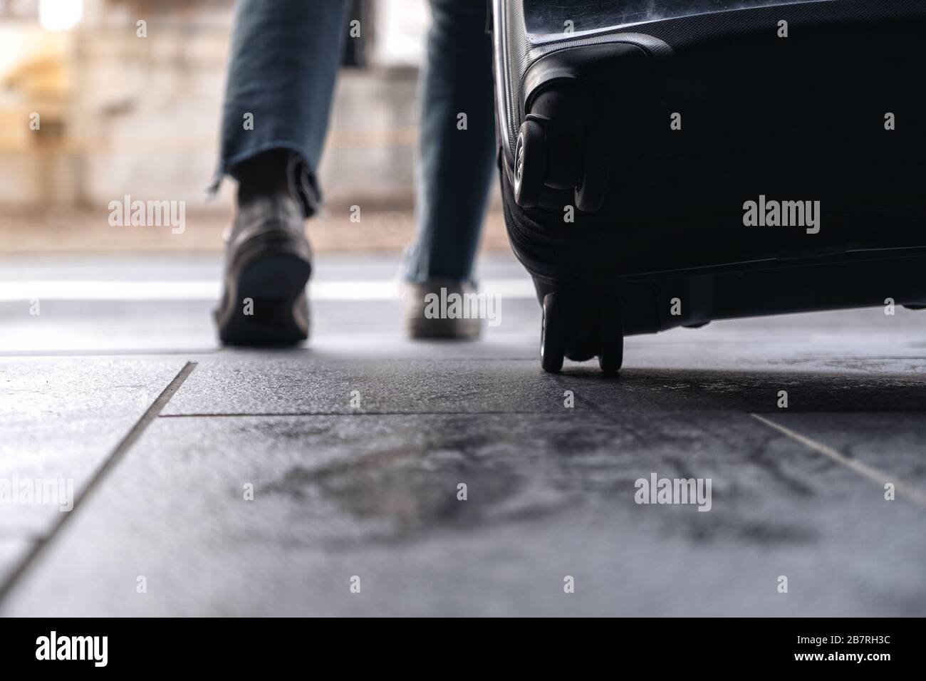 Immagine di primo piano dei piedi di una donna mentre si viaggia e trascinando un bagaglio nero all'aperto Foto Stock