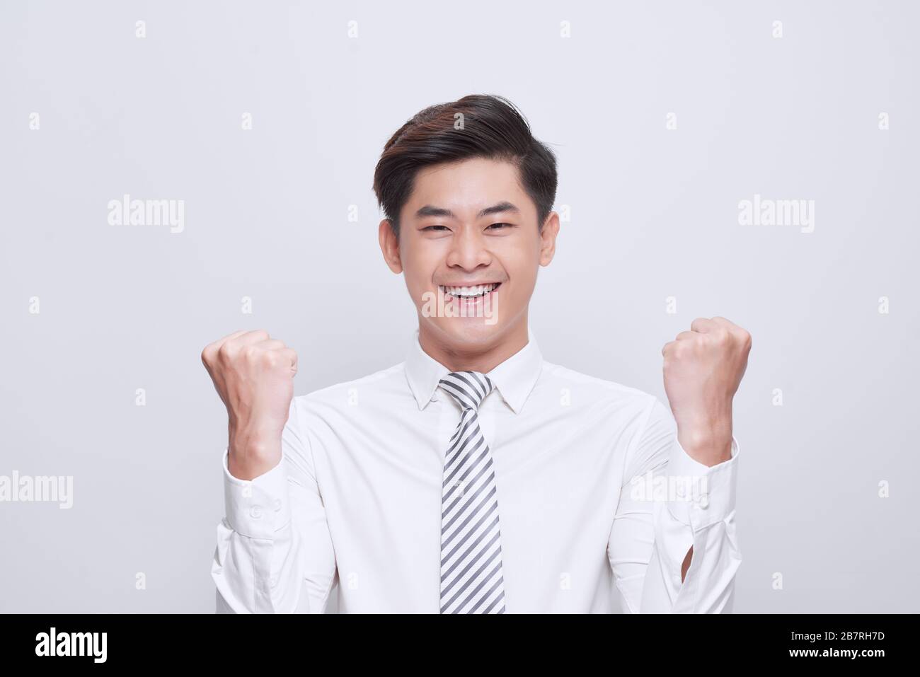 Ritratto di uomo vittorioso che guarda in alto mentre si alza su sfondo bianco e festeggia con pugni in aria Foto Stock