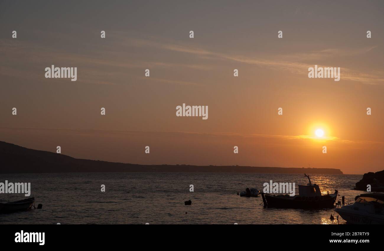 Tramonto colorato nel porto di Santorini Grecia Silhouette di barca da pesca con il sole basso nel cielo al tramonto e cielo giallo dorato Foto Stock