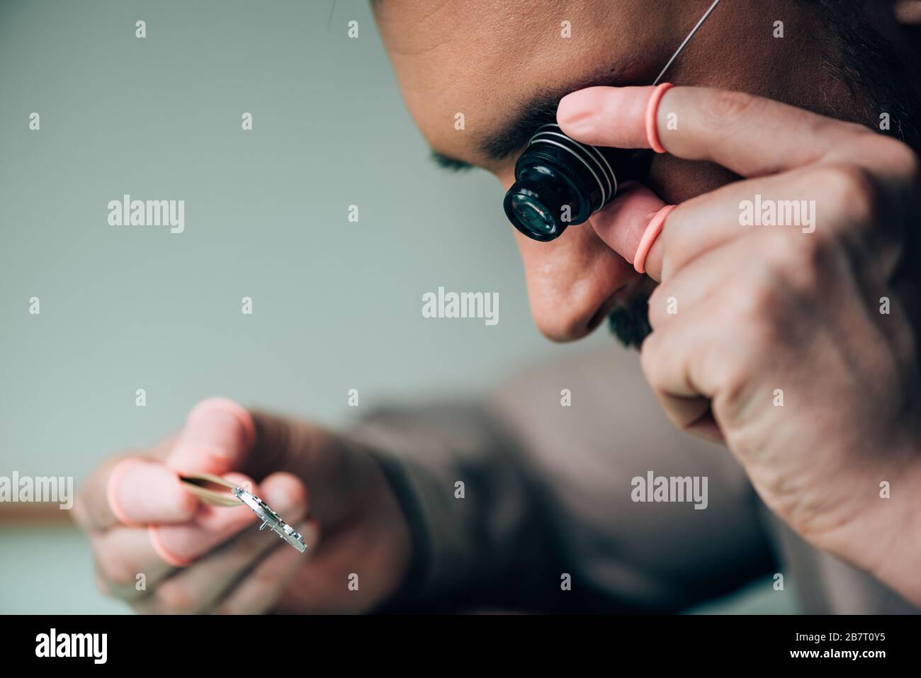 Vista laterale dell'orologiaio con le dita in lattice che tengono il loupe  degli occhiali e la parte dell'orologio Foto stock - Alamy