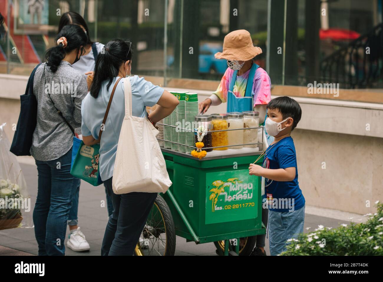 Una famiglia acquista un gelato su Ratchadamri Road, Bangkok, Thailandia. Tutti indossano una maschera protettiva contro il virus. Foto Stock