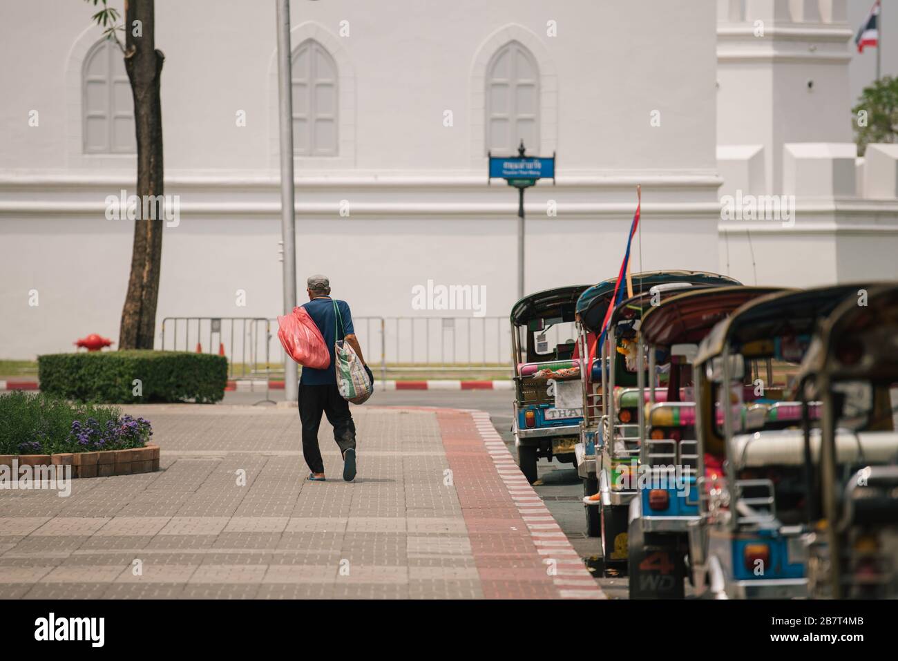 Un uomo senza tetto passa davanti a una fila di taxi vuoti accanto al Grand Palace di Bangkok, Thailandia. Le strade sono vuote senza i turisti regolari. Foto Stock