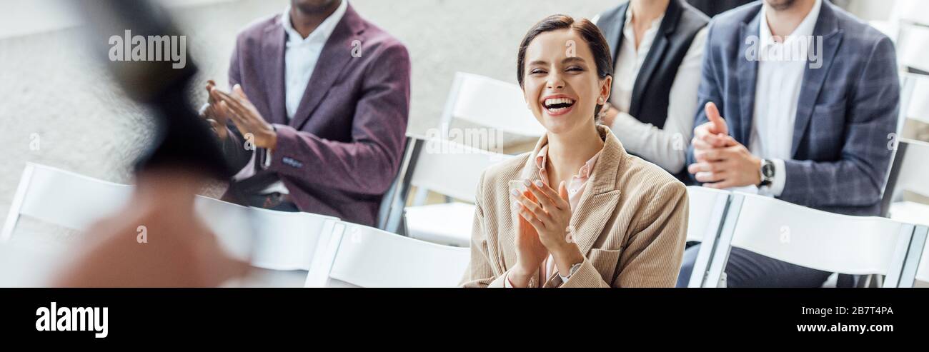 foto panoramica di una donna d'affari sorridente e applaudiente durante la conferenza Foto Stock
