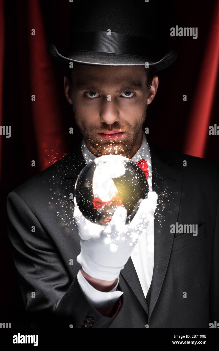 mago professionista che tiene palla magica con una luminosa illustrazione in circo con tende rosse Foto Stock