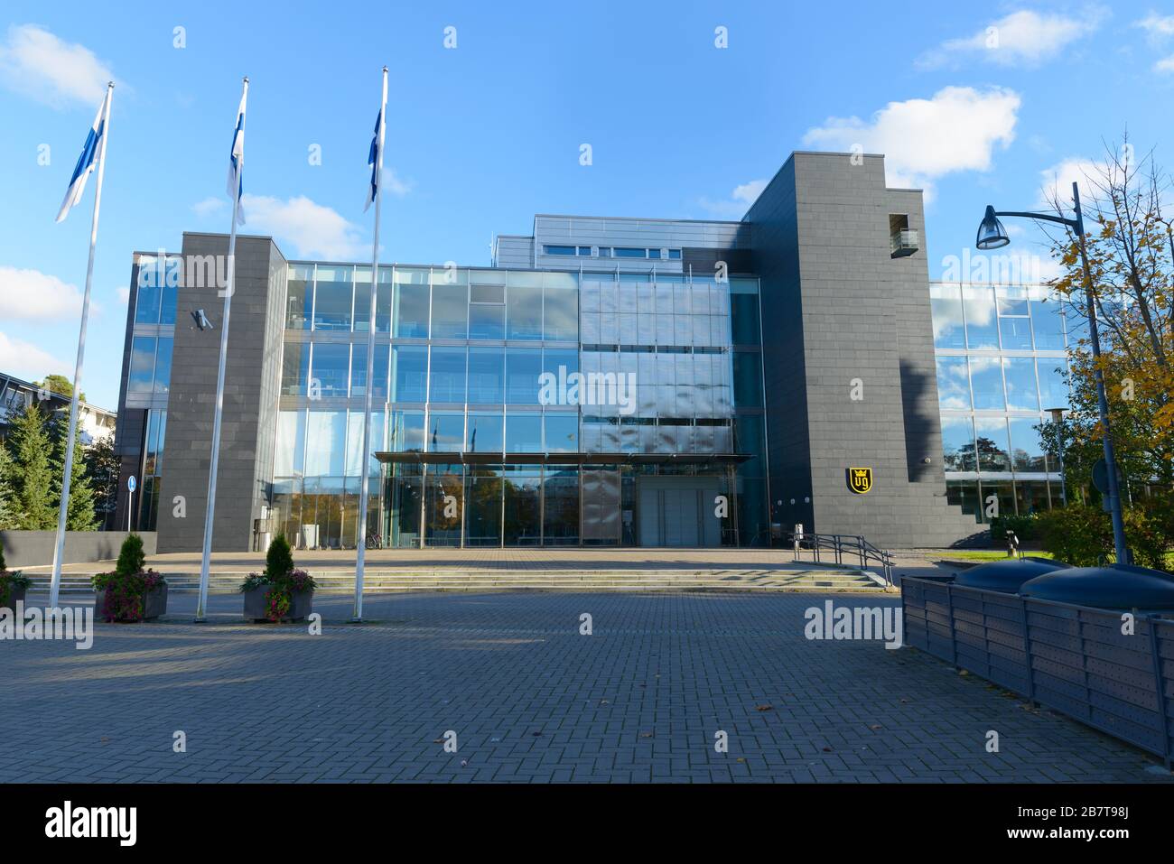 Ingresso di un moderno edificio della città di Naantali con tre pali della bandiera finlandese di fronte Foto Stock