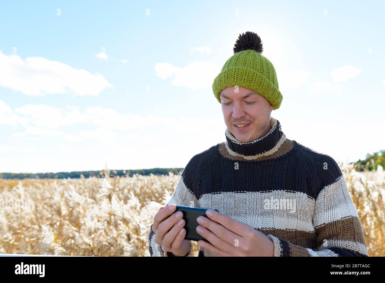 Felice giovane bell'uomo che usa il telefono contro la vista panoramica del campo di bullrush autunno Foto Stock