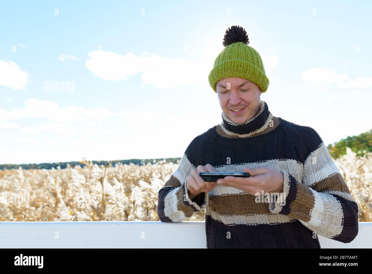 Felice giovane bell'uomo che usa il telefono contro la vista panoramica del campo di bullrush autunno Foto Stock