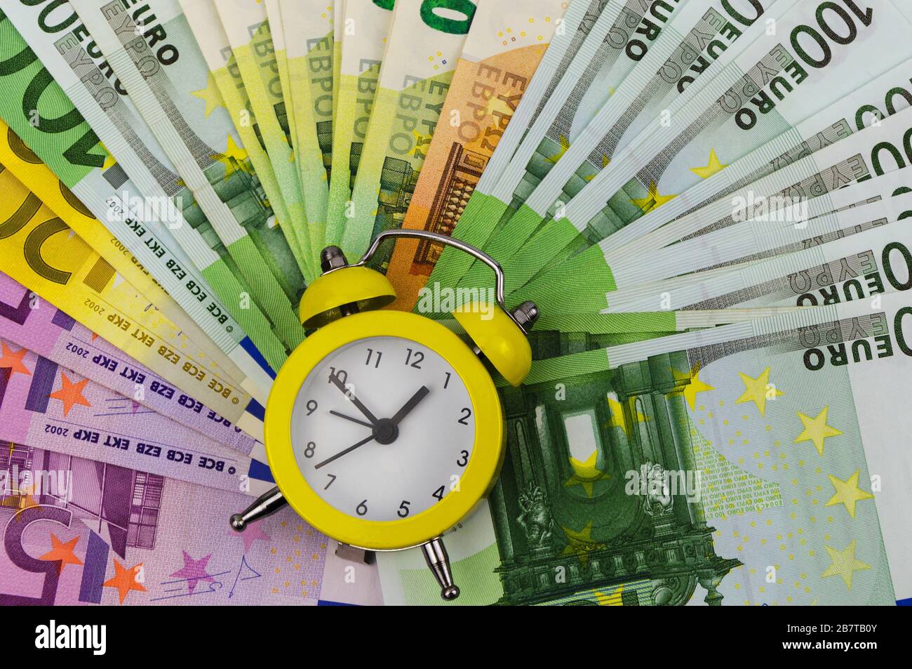 Sveglia gialla e banconote in euro di diverse denominazioni Foto Stock