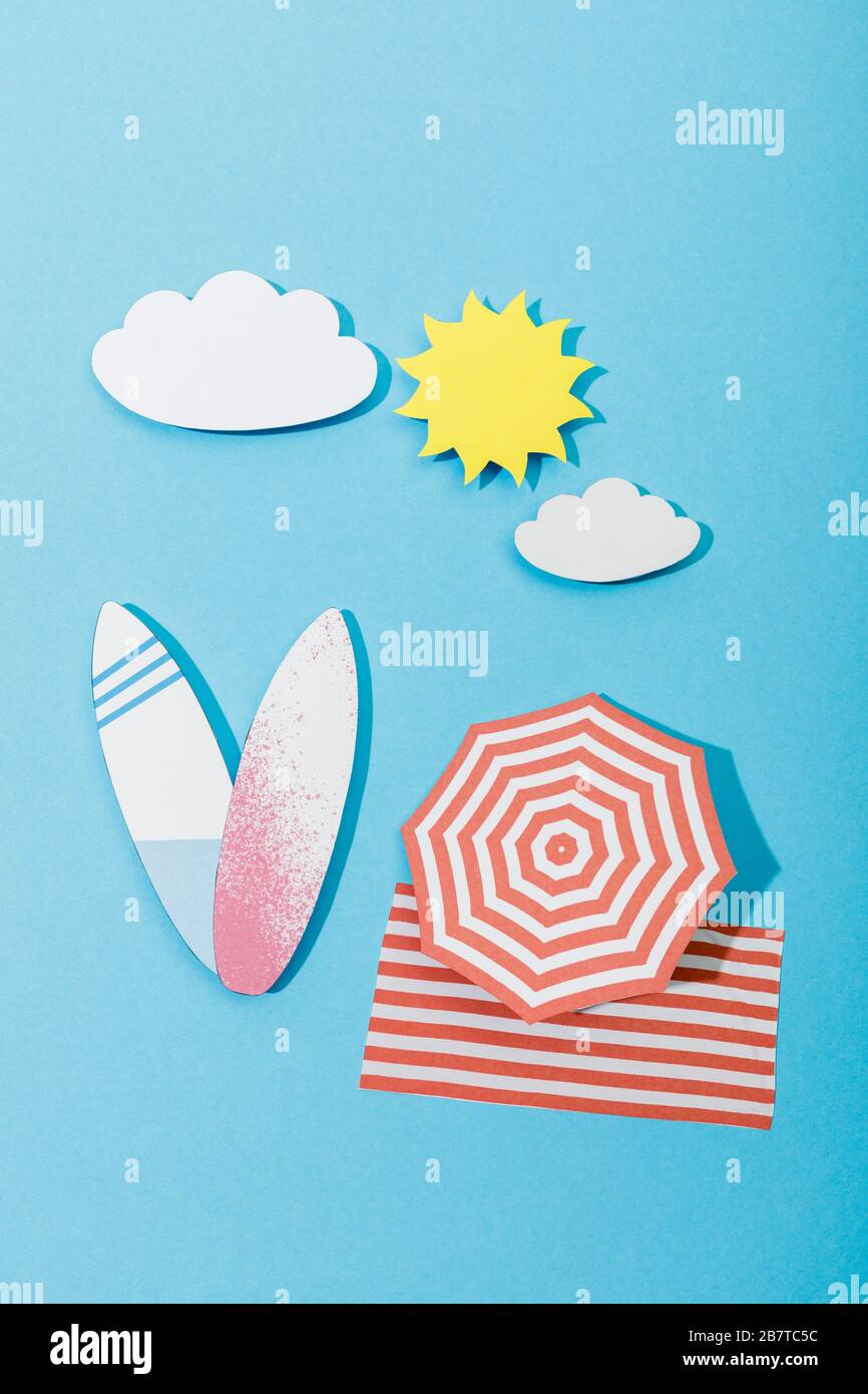 Vista dall'alto della spiaggia tagliata di carta con tavole da surf, ombrello e coperta su sfondo blu Foto Stock