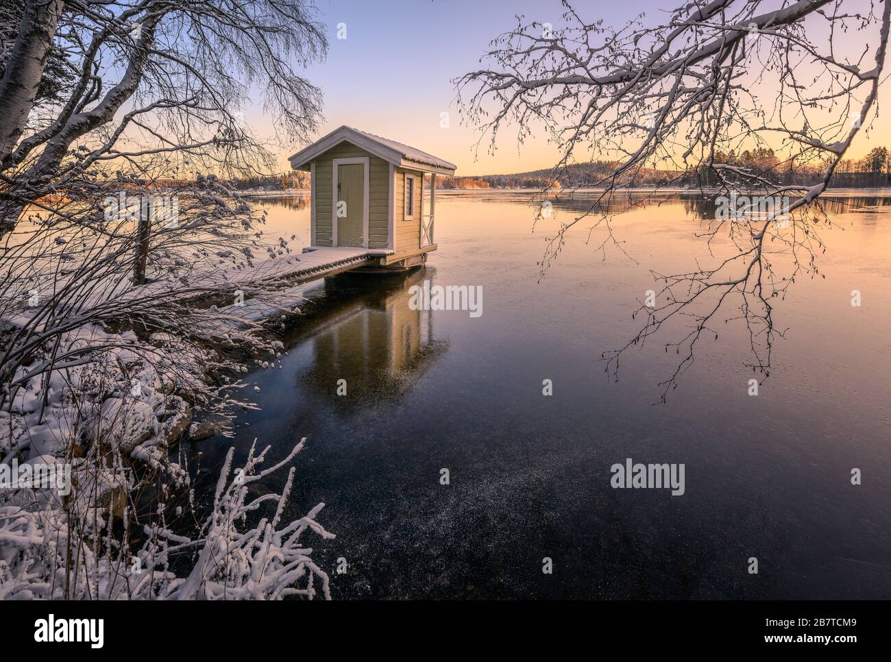Paesaggio invernale panoramico con tramonto e cottage accogliente sul lago ghiacciato e tranquillo in Finlandia Foto Stock