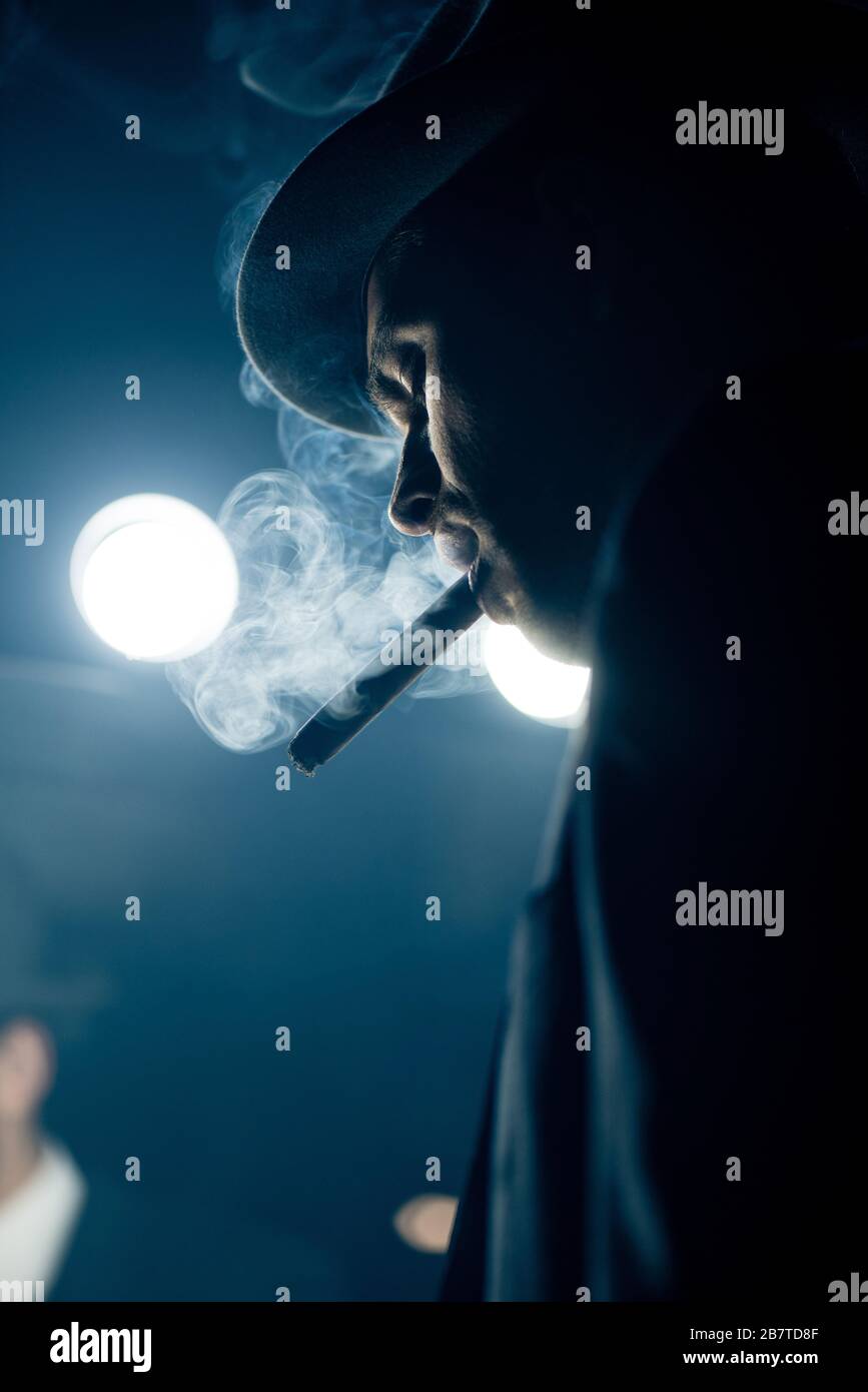 Vista a bassa angolazione del sigaro per fumatori mafioso al buio Foto Stock