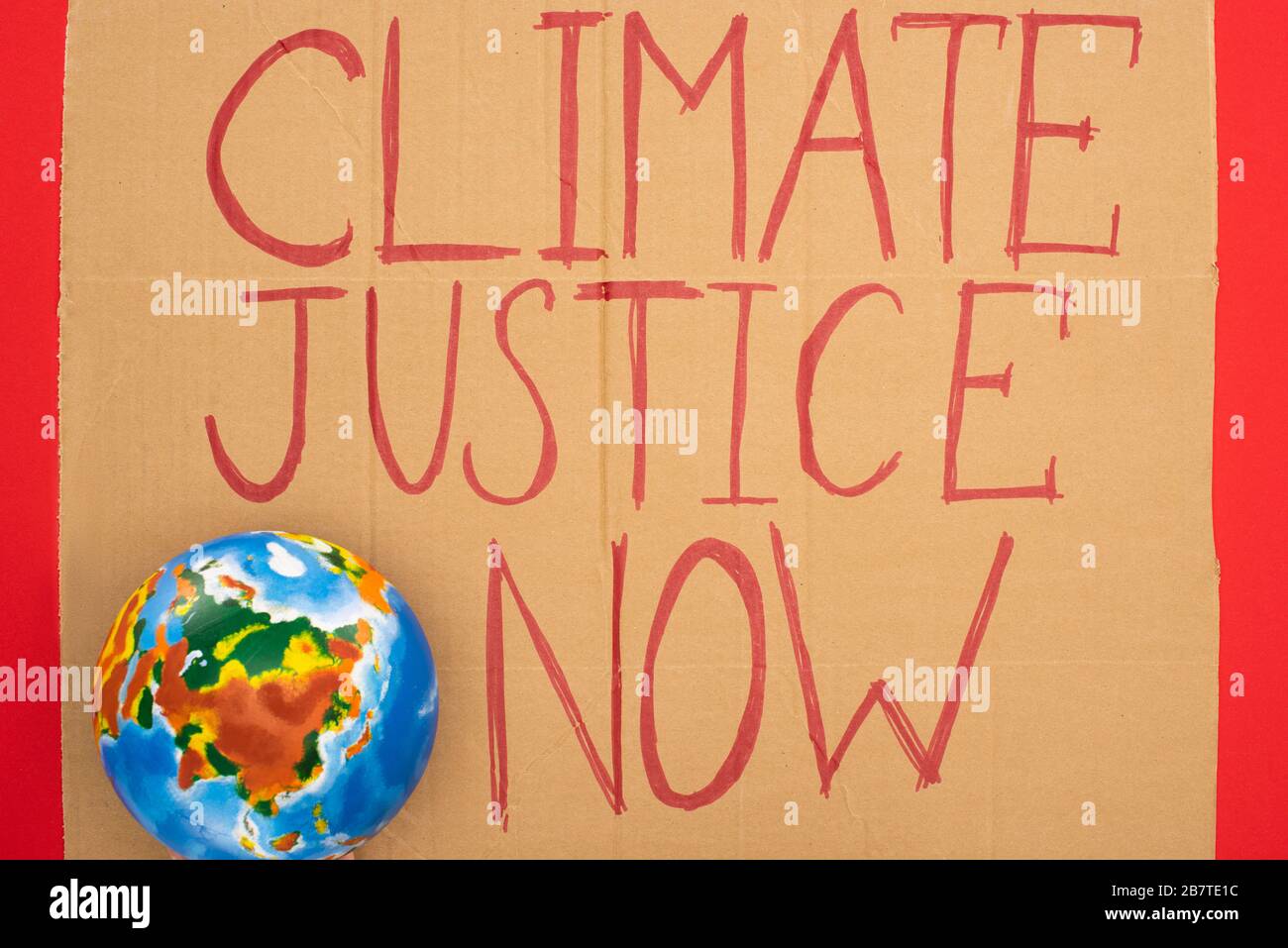 Vista superiore del globo e cartello con giustizia climatica ora scritta su sfondo rosso, concetto di riscaldamento globale Foto Stock