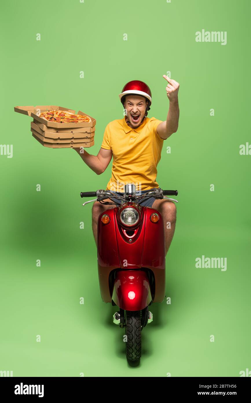 uomo eccitato in uniforme gialla con bocca aperta sullo scooter che  consegna la pizza e che mostra il dito medio sul verde Foto stock - Alamy