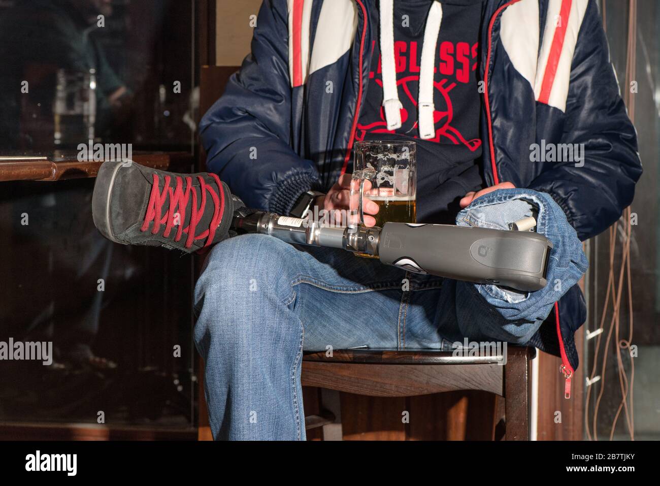 Uomo con amputazione e protesi seduto su un pub e bere una birra alla spina. Foto Stock