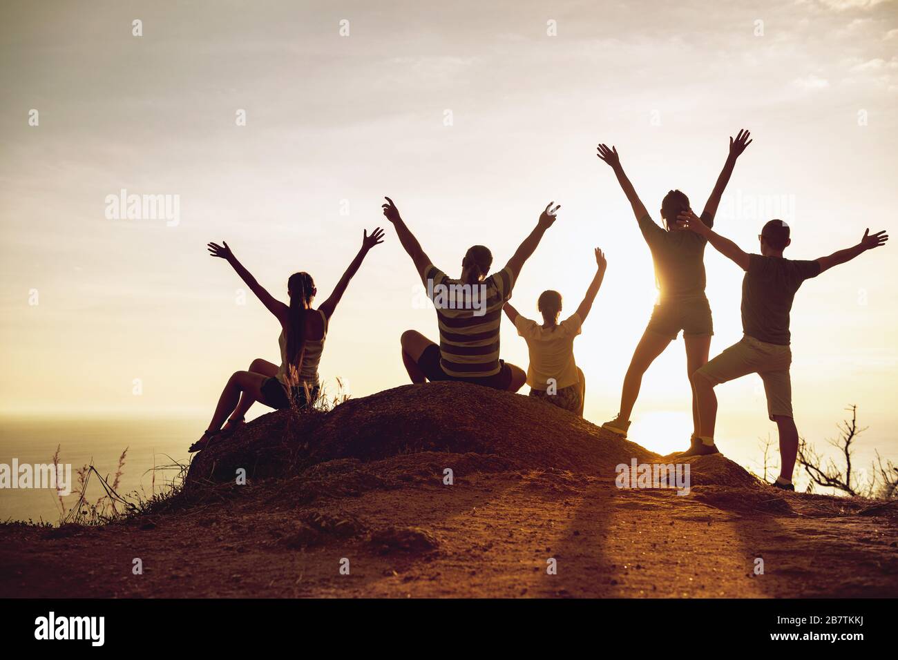 Gruppo di turisti felici si alza e si siede con le braccia sollevate al tramonto e divertirsi Foto Stock
