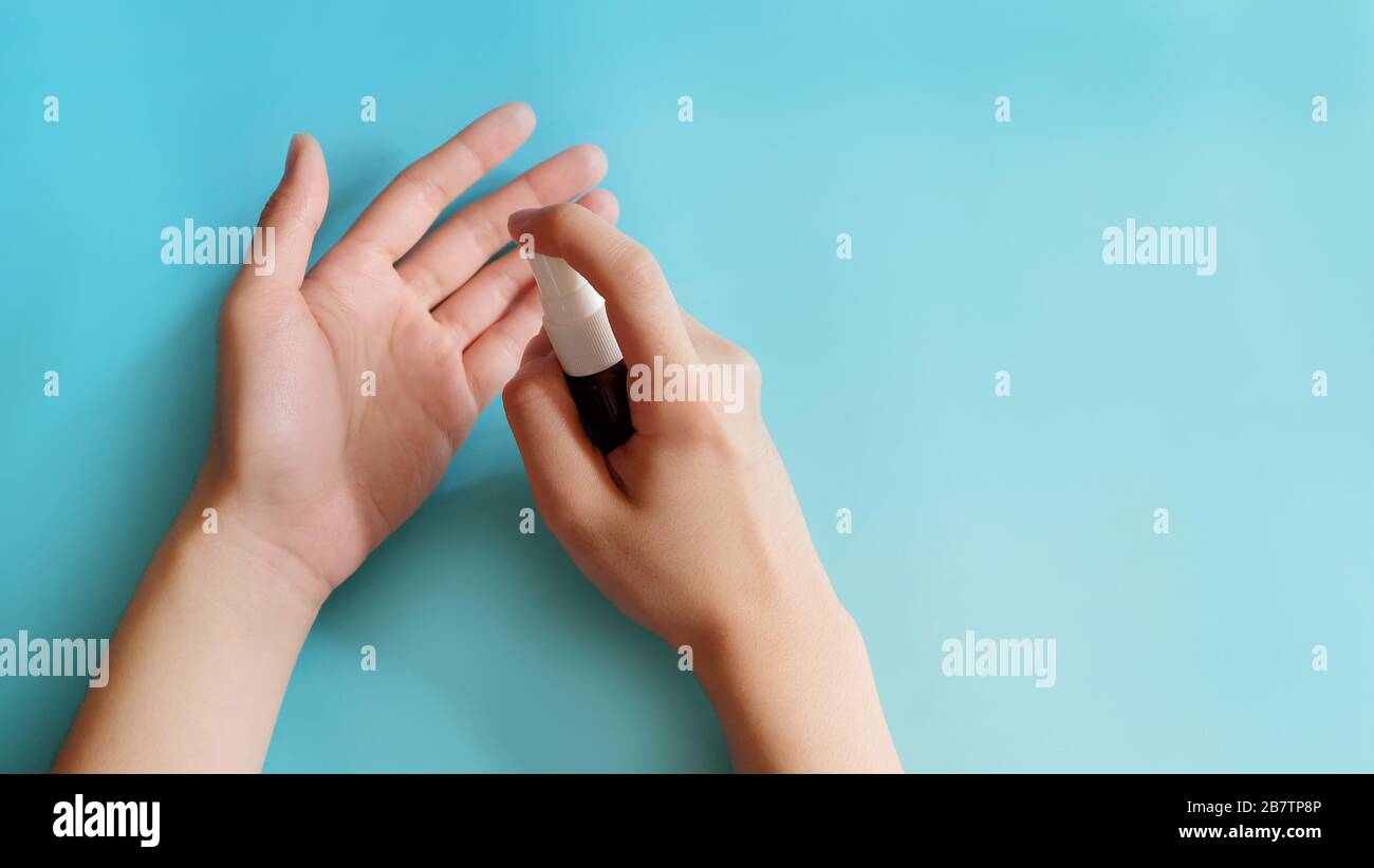 Una mano che tiene un piccolo flacone spray, spruzzando il contenuto verso l'altro palmo, a distanza ravvicinata. Foto Stock